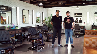 Two barbers stand for a portrait in their shop. 