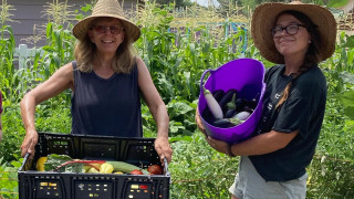 Two women hold containers full of vegetables. 