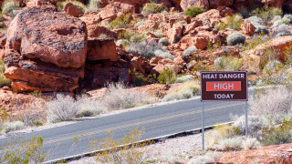 A sign that says Heat Danger High Today stands alongside a desert road.
