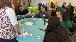 A group of people laugh around a pipe cleaner structure. 