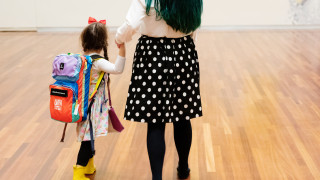 A girl wearing a backpack holds the hand of an adult while exploring a museum.