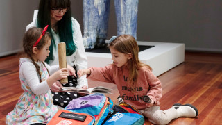 A family sits in a gallery at UMFA and explores the contents of a sensory bag.
