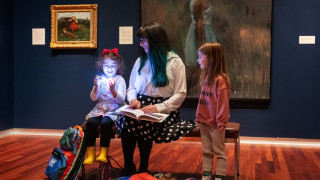 A family sits on a bench in a gallery at UMFA with a sensory bag