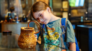 A young girl examines a pitch basket with a microscope, both provided in a sensory bag at NHMU.