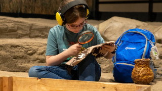 A girl examines a small Navajo rug using a magnifying glass provided by a sensory bag at NHMU.