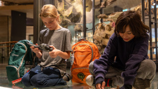Children sit in a gallery at NHMU using contents of a sensory bag.