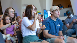 Two people sample small muffins inside NHMU.