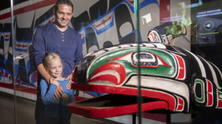 A father and daughter look at an indigenous Orca sculpture through a glass case.