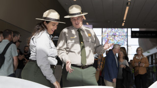 Two National Park Service employees learn about an Allosaurus skeleton inside the Salt Lake City International Airport.