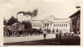 A historic black and white photo of a wagon train arriving at the University of Utah.