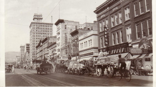 A historic black and white photo of a wagon train in downtown Salt Lake City.
