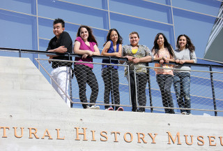 Students stand at a railing in front of a museum.