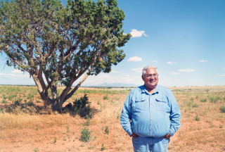 A man stands in the desert next to a tree. 