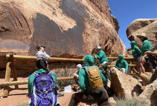A group of people in green shirts look at a petoglyph site