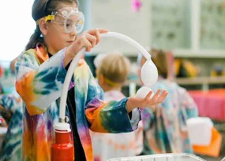 A child conducts an experiment while wearing a colorful lab coat.