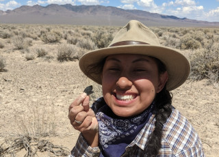 Olivera smiles in the desert as she holds up a small, ancient artifact.