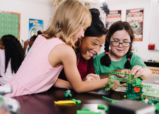 Two girl scouts and a girl scout leader build a small machine with connectable bricks.