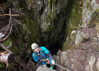 A man rappels into a cave. 