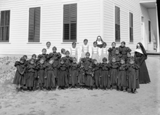 A group photo of young students in formal dress outside the school