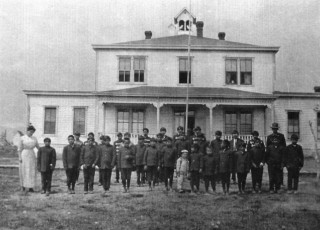 A black and white photo of young boys standing in front of a large white residential building