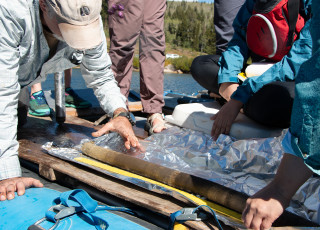 Scientist on a raft examine a tube-shaped lake core pulled from the lake bed. 