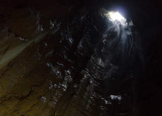 A small figure rappels into a deep cavern as viewed from far below. 