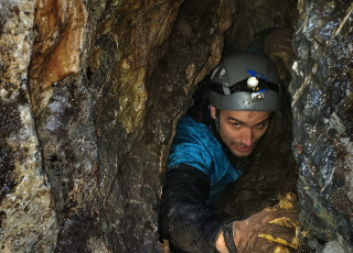 A scientist squeezes through a narrow entrance to a cave. 