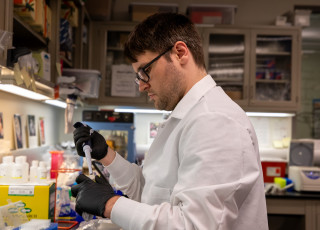 a person in a lab coat and gloves holding a pipette