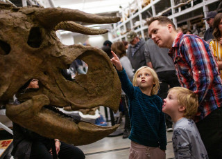 a person and two children looking at a dinosaur head