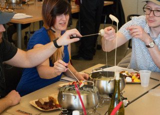 Three people pull cheese fondue out of a pot on a table