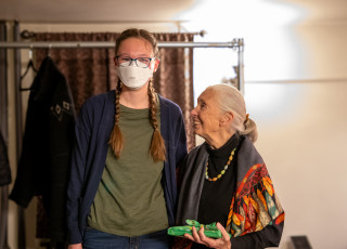 A young person in a mask with braids stands next to an older woman with her hair in a ponytail