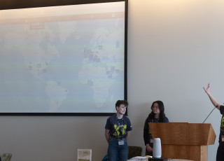 3 people in green shirts point to a map on a projector screen
