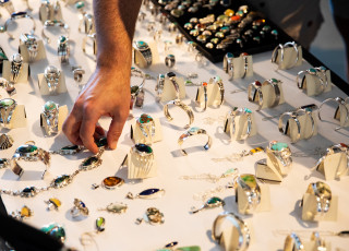 A hand sorts silver jewelry on a white table top