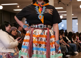 A young woman models a black top with patterned skirt and Native American jewelry