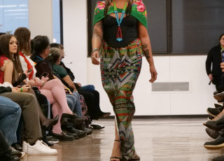 A woman models a black top with a colorful skirt and shawl 