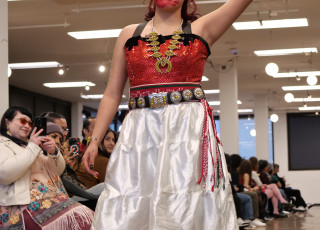 A young woman raises her arm with red paint on her face wearing a red top with white skirt and 