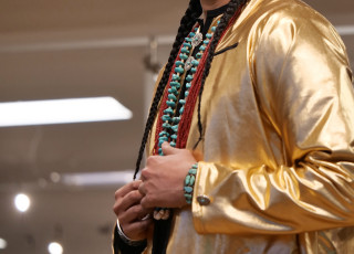 A man models a gold jacket with Native American jewelry and red face paint