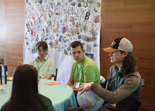 Teens sit at a table while one holds a globe ball