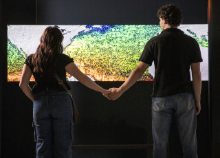 2 people stand holding hands in front of a digital map
