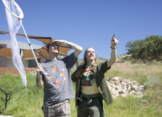 2 people look towards the sky, one points and the other holds a large net