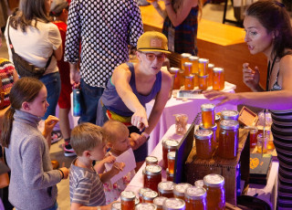 A person and 3 children look at honey from a BugFest vendor