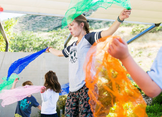 A yoga instructor leads kids in a dance with colorful scarves. 