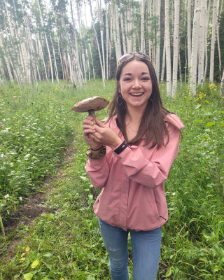 Cosette stands in a forest holding a mushroom.